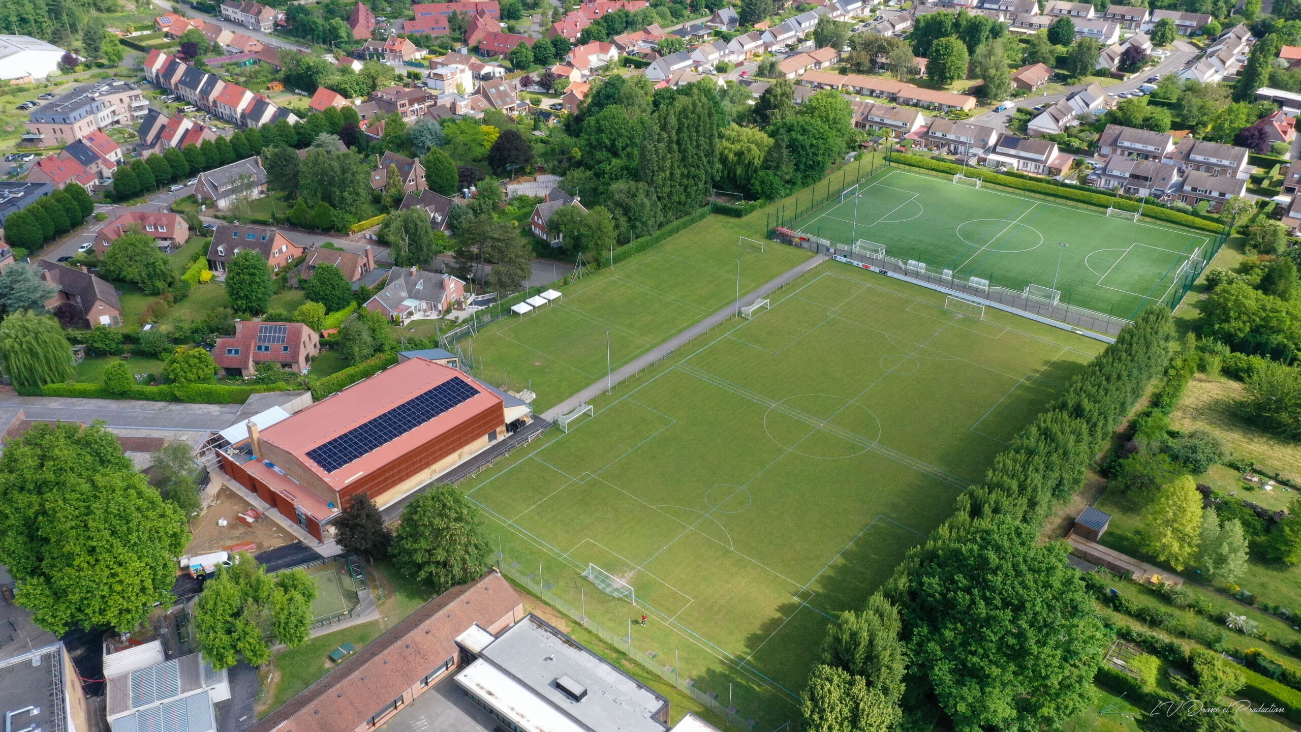 Terrain de football extérieur avec éclairage, situé dans un environnement résidentiel verdoyant.
